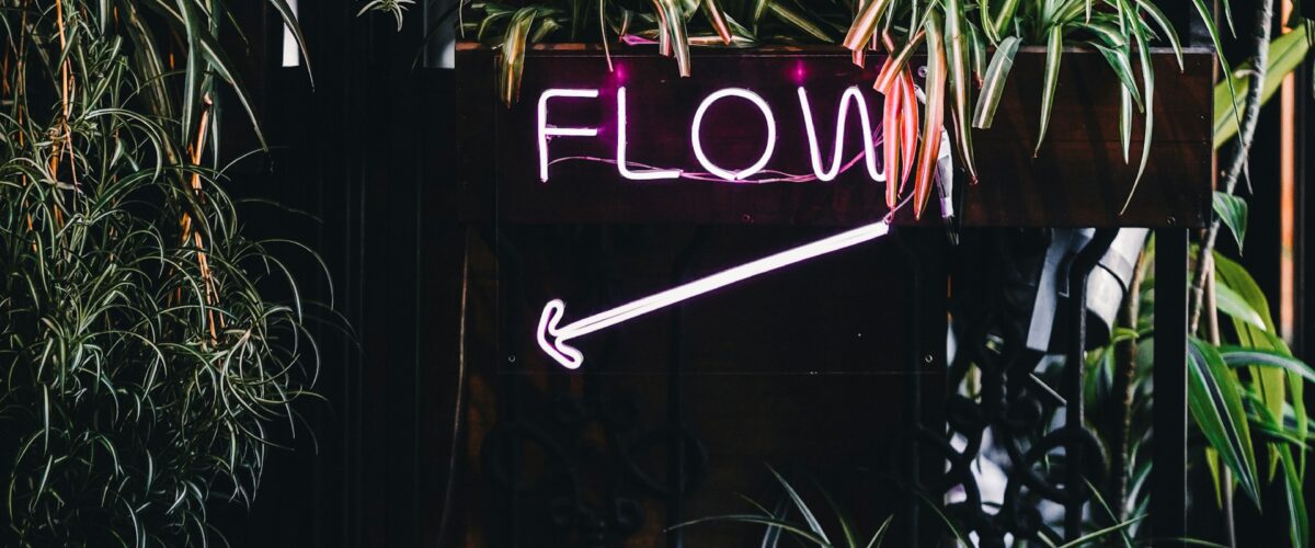 A neon sign that says "flow". There are a bunch of potted plants surrounding it