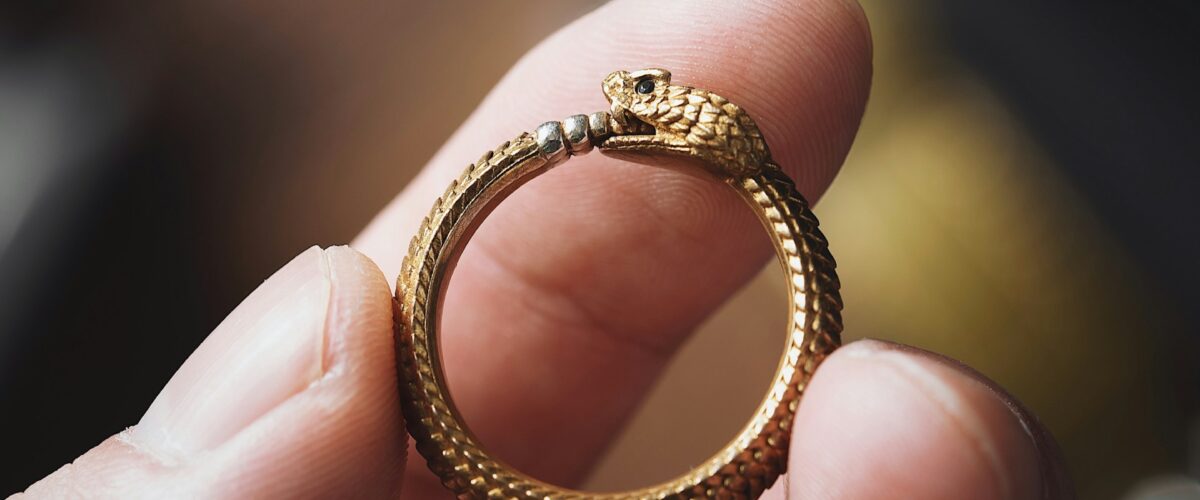 closeup of hands holding a gold ouroboro ring (a snake eating its own tail)