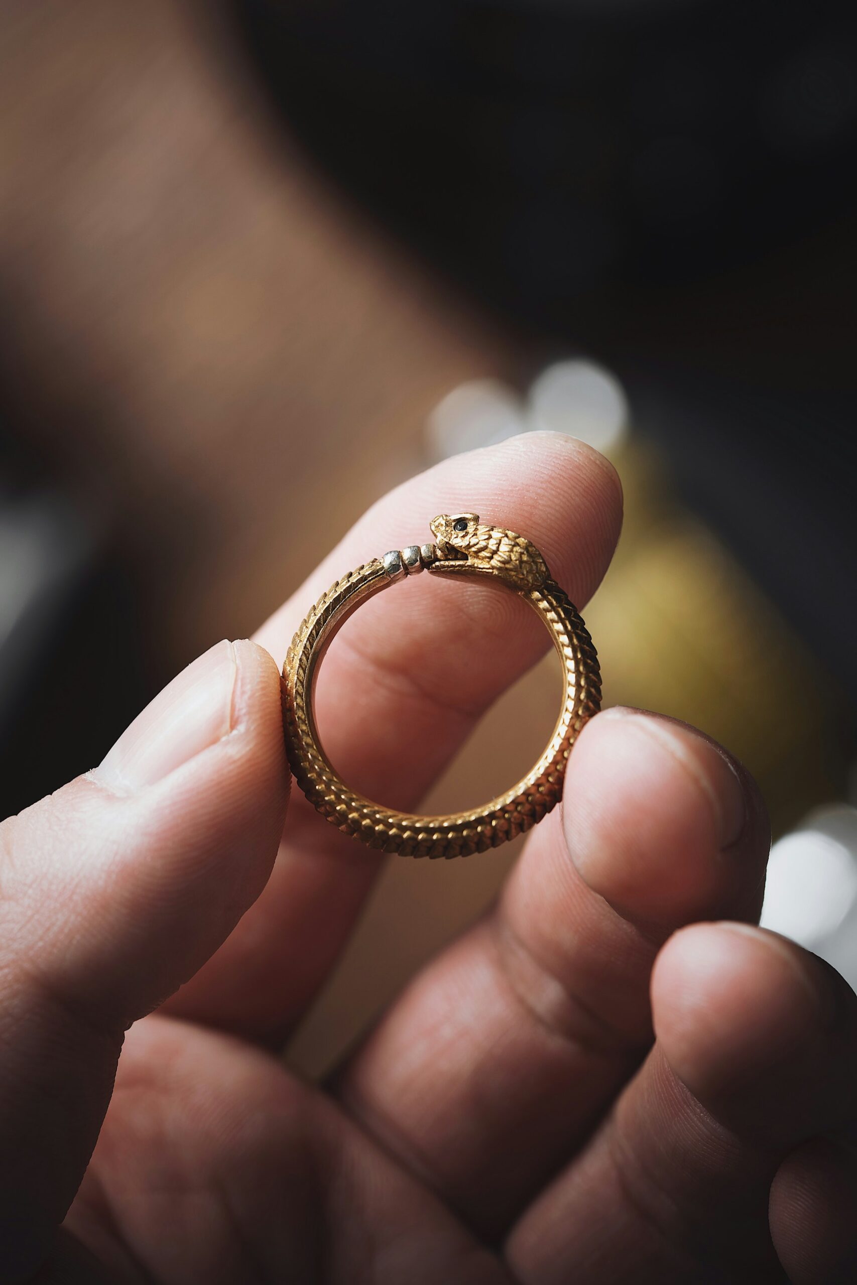 closeup of hands holding a gold ouroboro ring (a snake eating its own tail)